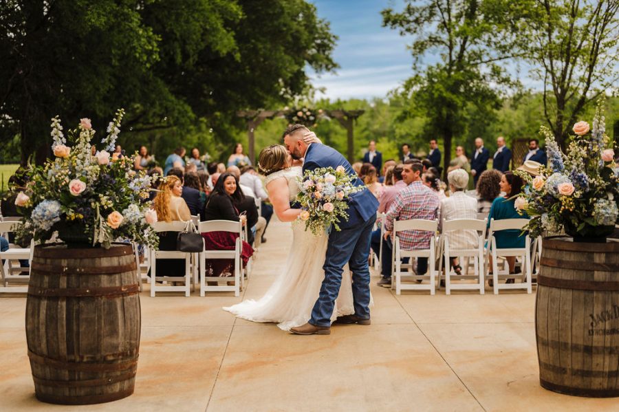 newlywed dip kiss in front of a beautiful outdoor ceremony spot surrounded by trees and greenery 